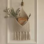 Macrame wall hanging with tassels and a plant on a neutral background