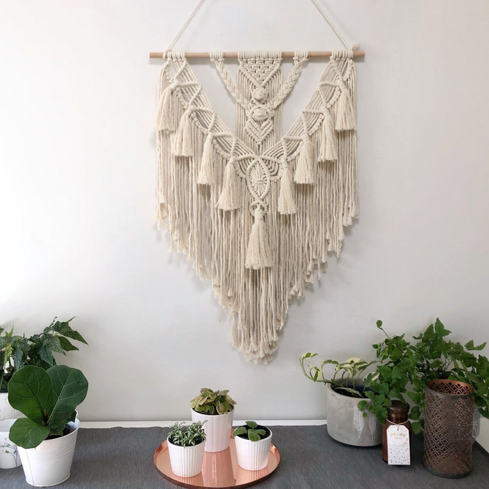 Macrame wall hanging above a table with potted plants on a white wall background