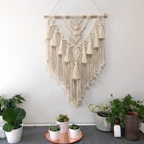 Macrame wall hanging above a table with potted plants on a white wall background