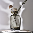 Clear glass vase with dried flowers on a light gray background