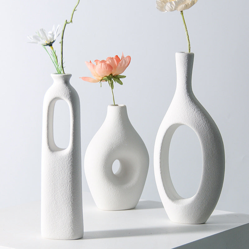 Minimalist white frosted ceramic vases with sculptural cutout designs.