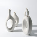 Set of four white ceramic vases with unique designs on a light gray background