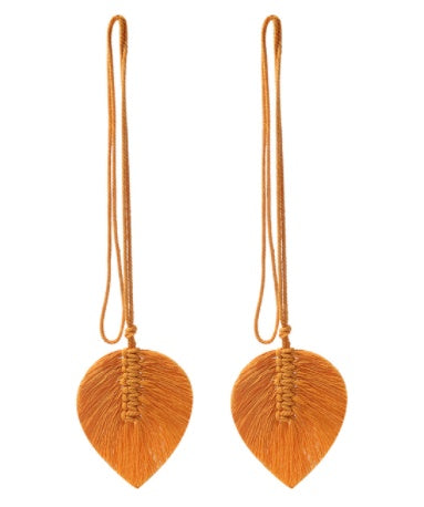Pair of orange leaf-shaped earrings with strings on a white background