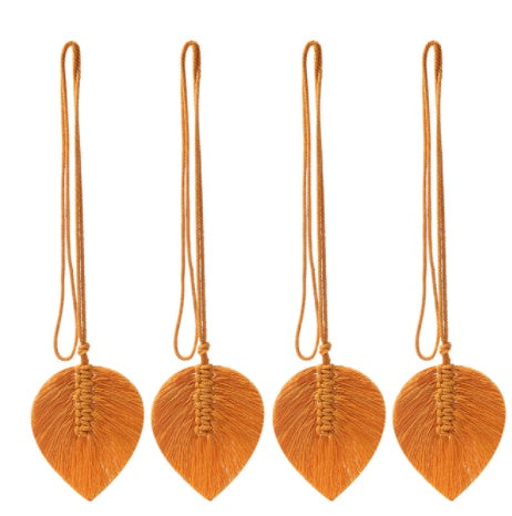 Four orange leaf-shaped macramé decorations with strings on a white background