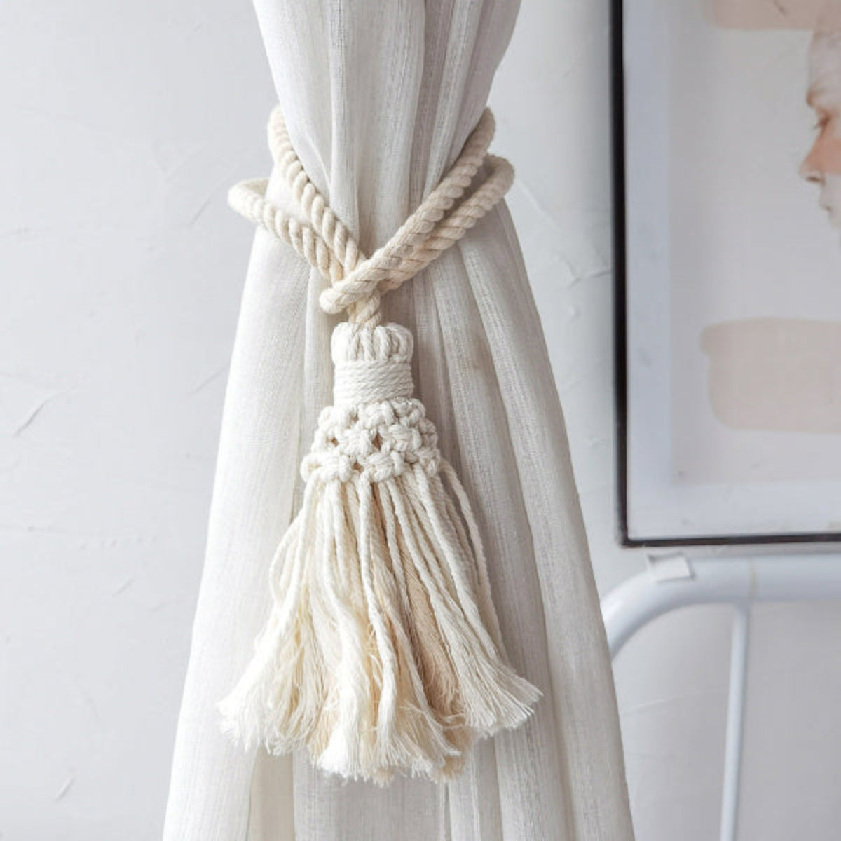 Curtain tieback with tassel attached to a sheer curtain in a room setting.
