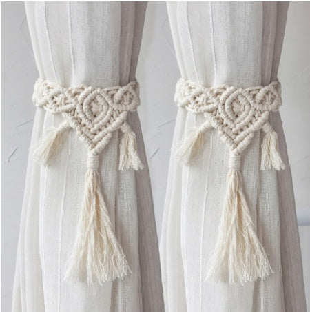 Two curtains with macrame tiebacks and tassels on a neutral background