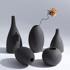 Set of black ceramic vases on a gray background with a bronze flower arrangement.