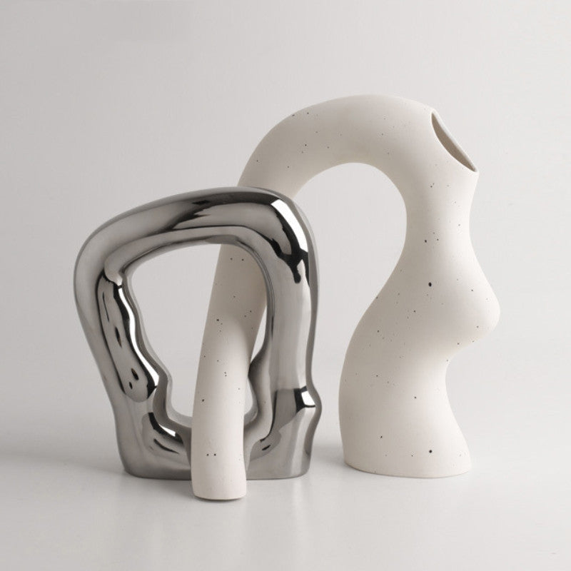 Two abstract ceramic sculptures, one silver and one white with speckles, on a light gray background.