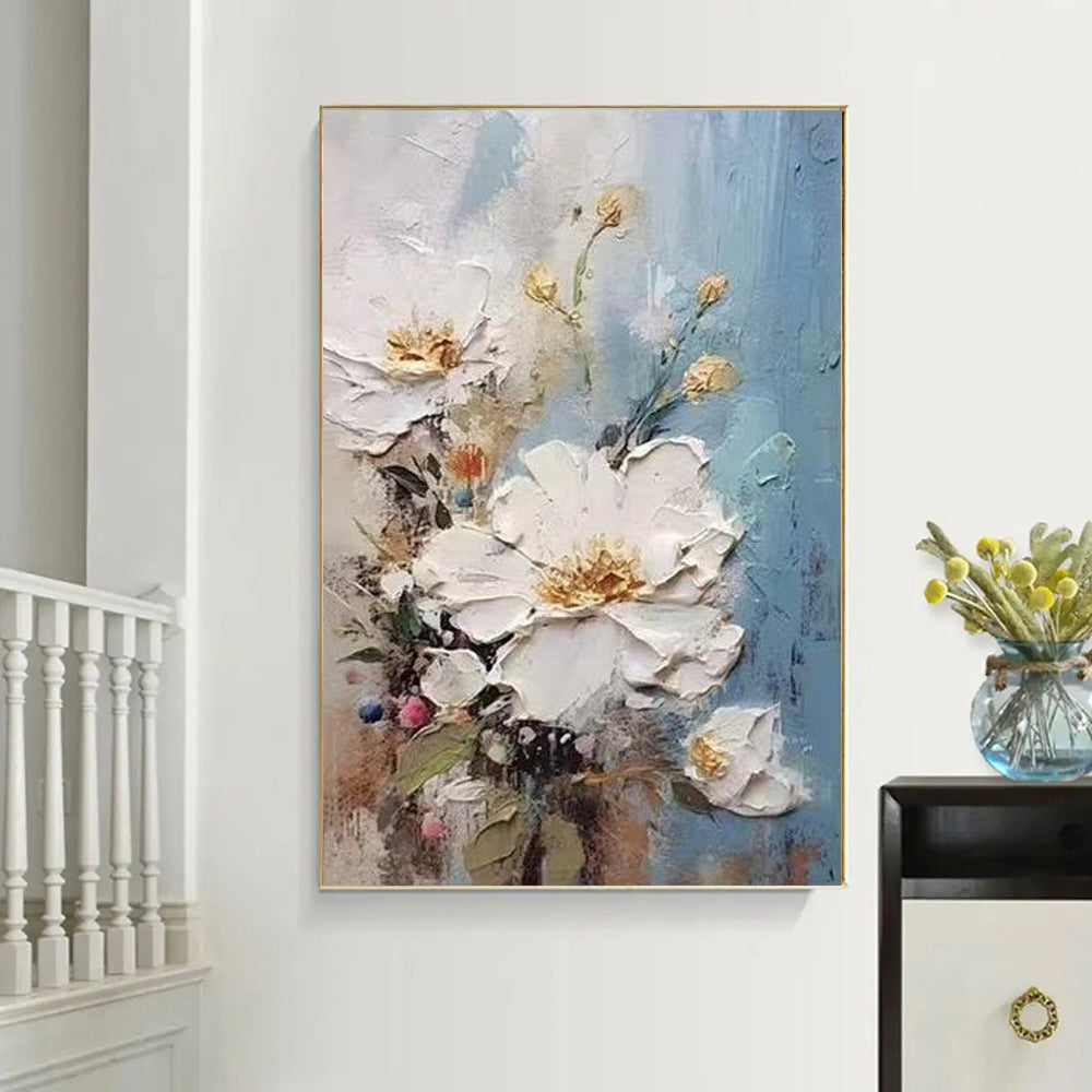 Floral painting on a wall with a vase of flowers on a table to the right.