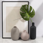 Three vases on a marble surface with a framed abstract artwork in the background. Miora Frosted Glass Ceramic Vase.