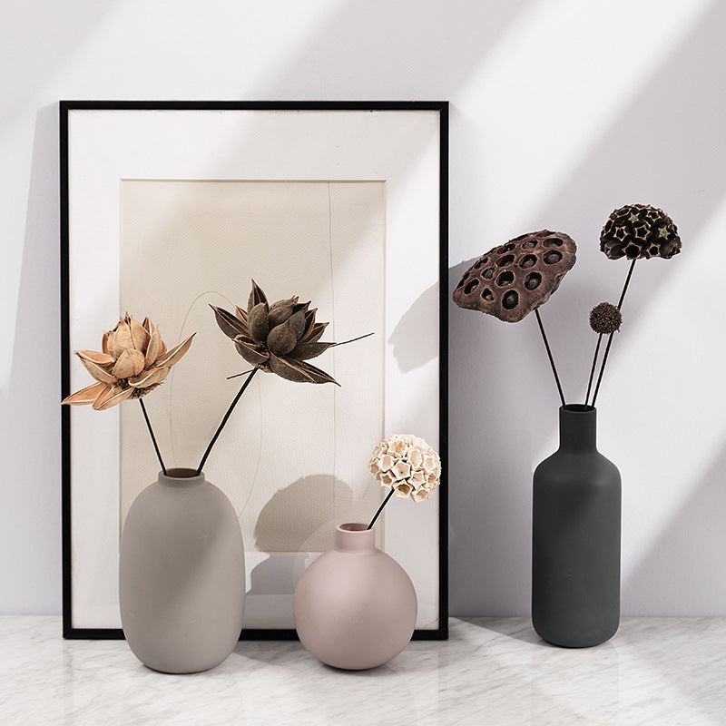 Three vases with dried flowers against a white wall with a framed picture.