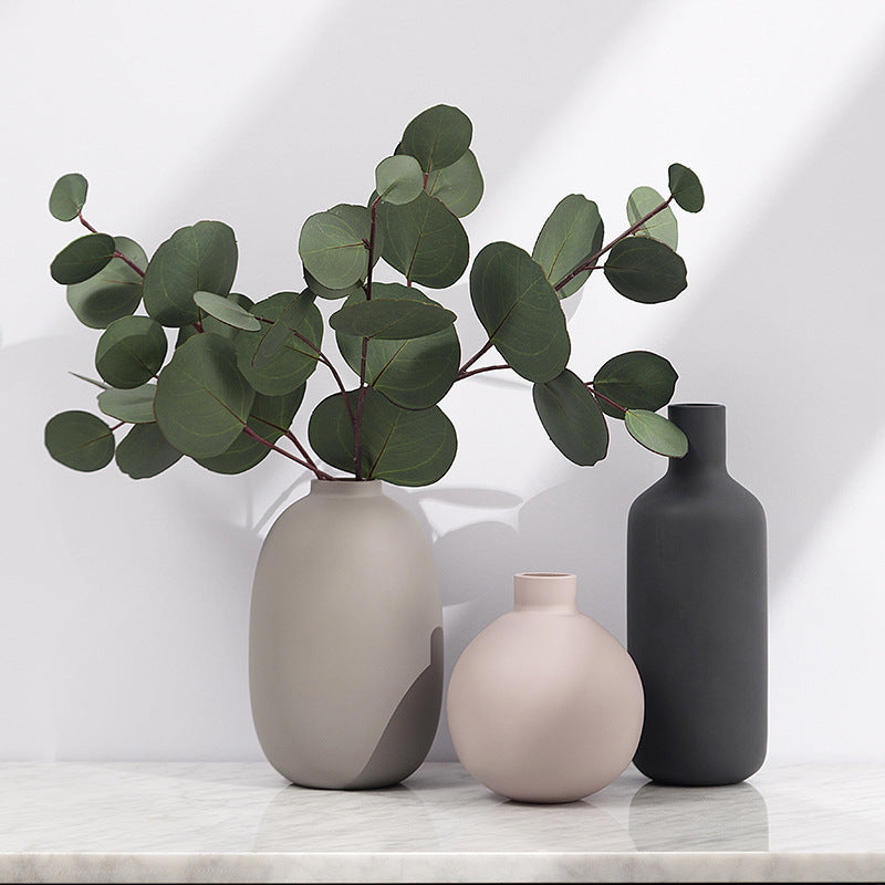Three vases of different shapes and colors with a branch of eucalyptus on a light background