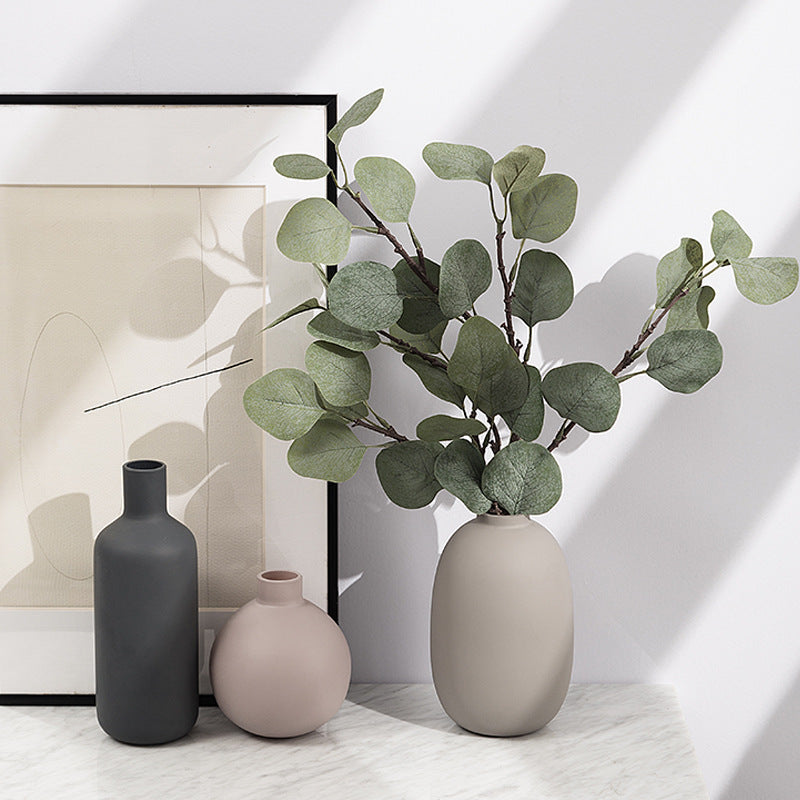 Decorative vases with a plant on a light surface, framed artwork in the background