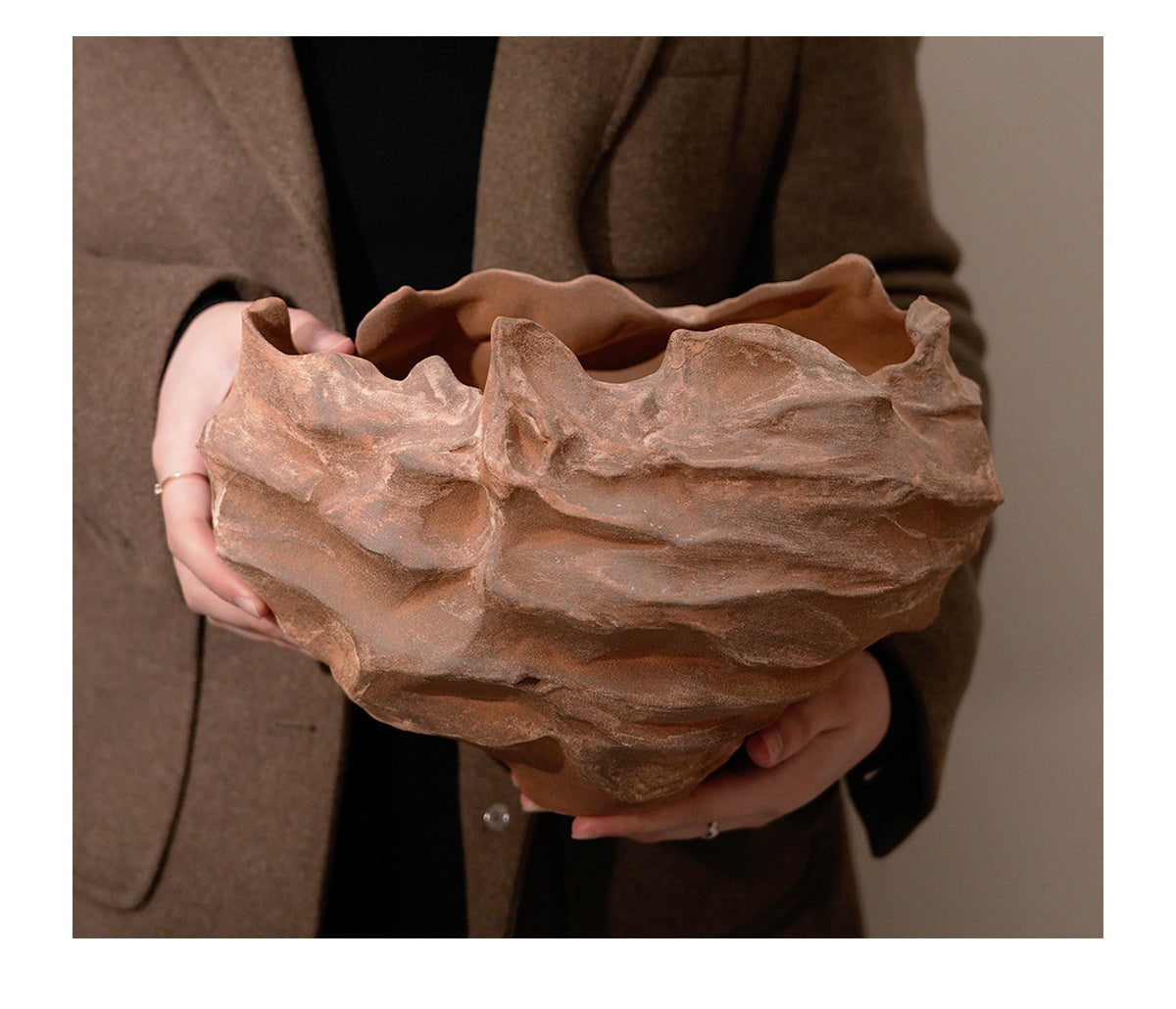 Person holding a large, textured terracotta pot against a neutral background