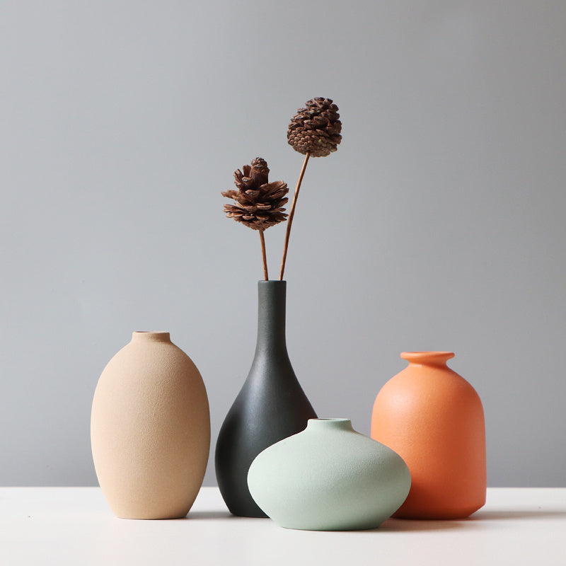Four ceramic vases in different colors with decorative elements on a plain background