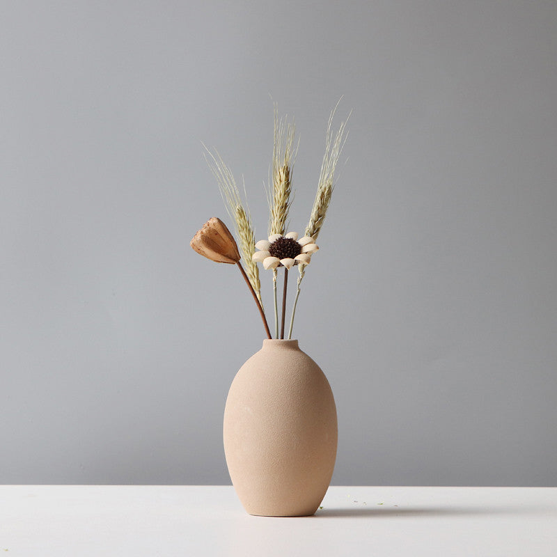 Beige ceramic vase with dried plants on a gray background