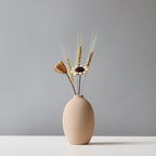 Beige ceramic vase with dried plants on a gray background