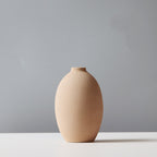 Beige ceramic vase on a white surface with a gray background