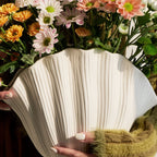 White shell-shaped vase with a bouquet of flowers in the background