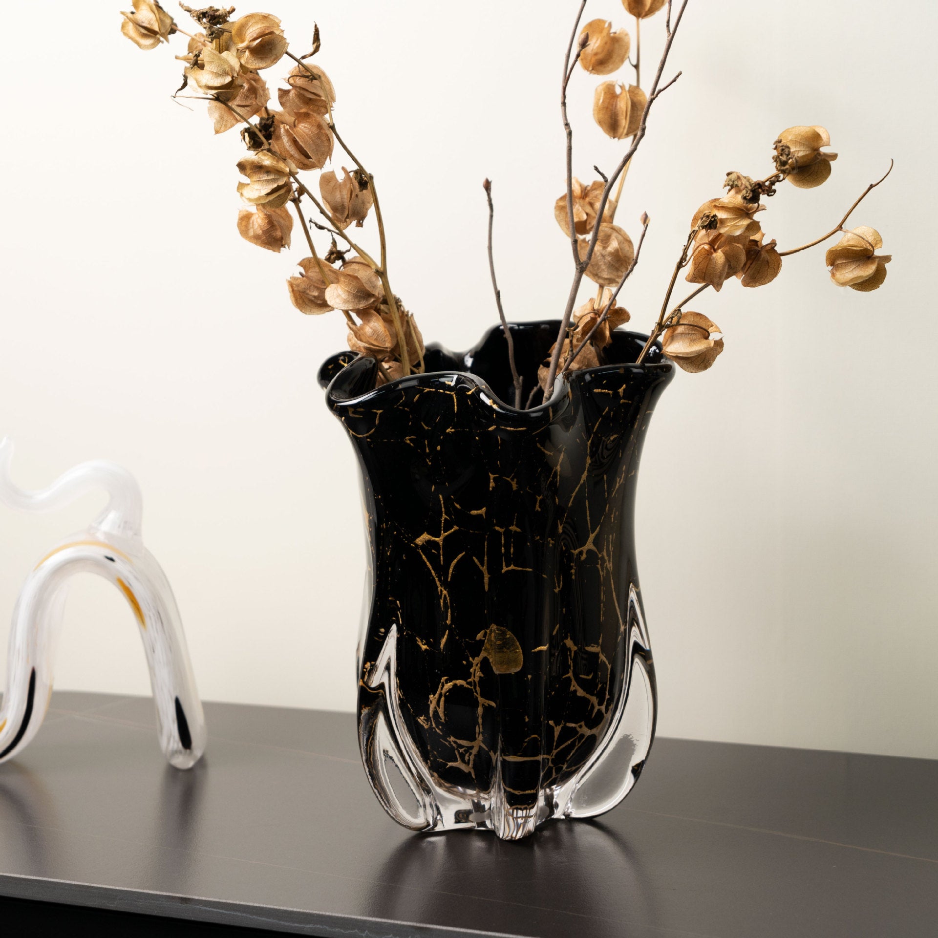 Black and gold vase with dried flowers on a reflective surface