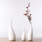 Three white ceramic vases of varying heights on a wooden surface with a plain background