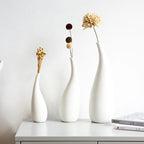Three white vases with dried flowers on a white surface