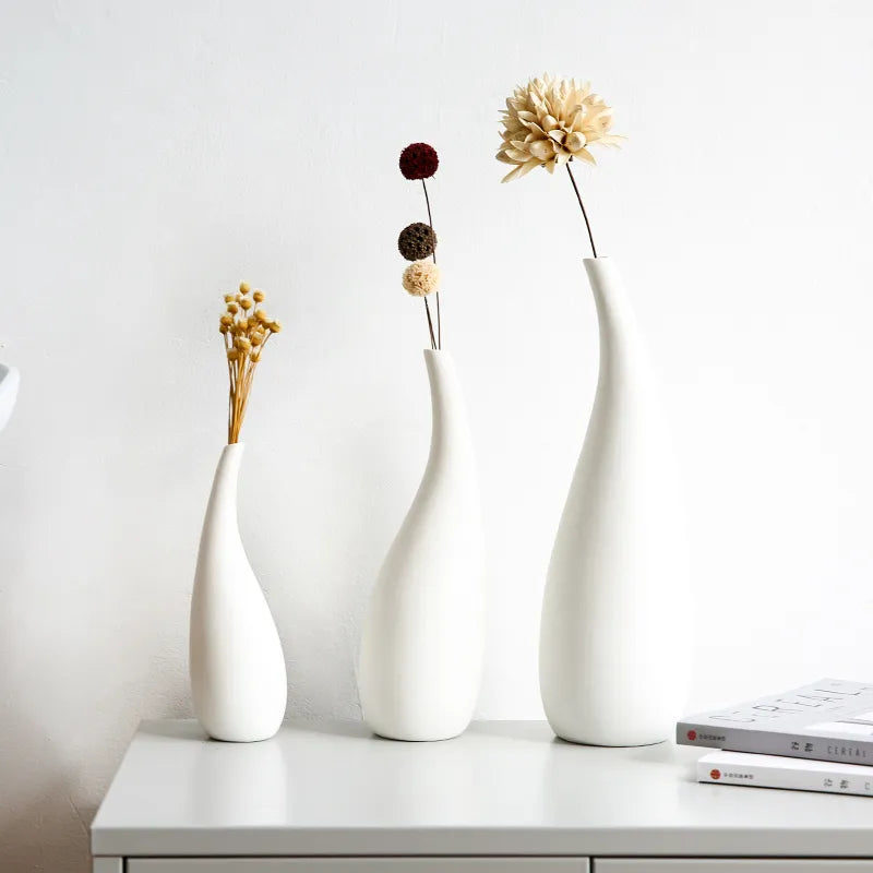 Three white vases with dried flowers on a white surface