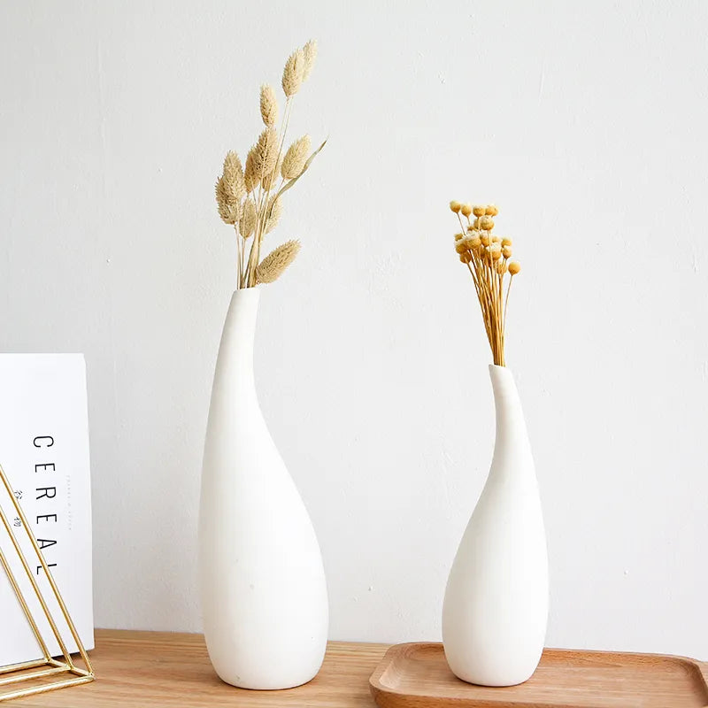 Two white vases with dried plants on a wooden surface against a light gray background